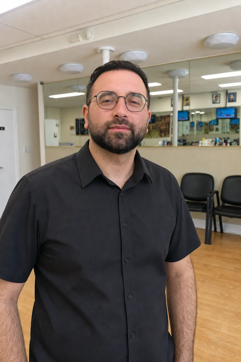 Ruben, head barber at Camp Ave Barbershop, standing in the shop in his black work shirt